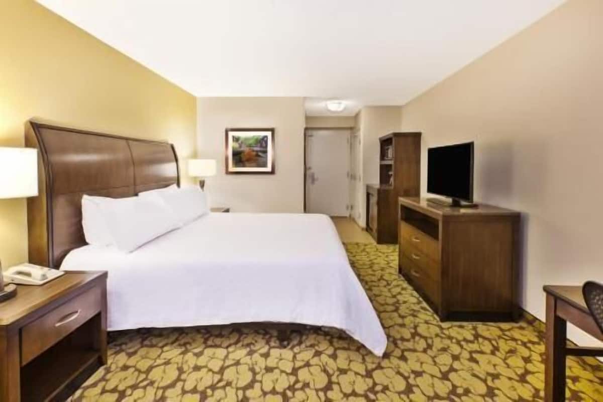 A hotel room with a bed, a desk with a lamp, a television, and a wardrobe.