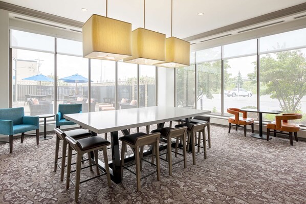 Conference room with a large table and six chairs, surrounded by a patterned carpet and natural light from large windows.