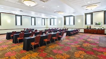 Un salón de conferencias con mesas y sillas, amplias ventanas y suelo alfombrado.