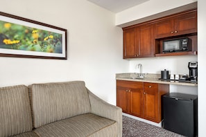 Cozy hotel room with a kitchenette, sofa, and framed artwork.