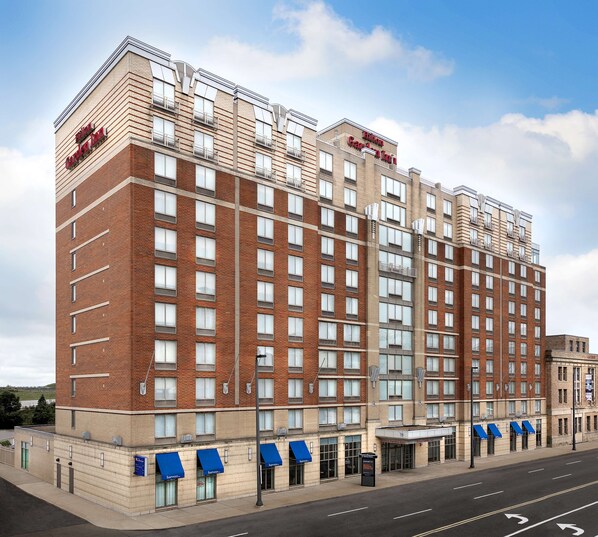 A multi-story hotel with a brick facade, large windows, and blue awnings. - Hilton Garden Inn Cleveland Downtown (Cleveland)