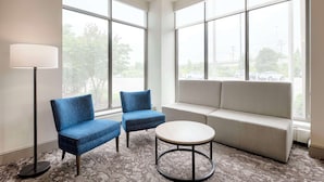 Une pièce moderne avec de grandes fenêtres, un canapé, deux fauteuils et une petite table ronde.