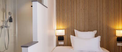 A hotel room with a shower, two bedside lamps, and a bed with white bedding.