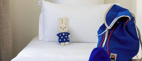 A bed with a white pillow, a stuffed bunny, a blue backpack, and a pair of sunglasses.