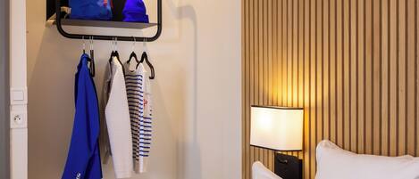 Een hotelkamer met een bed, een wandplank met kleding, een lamp en een houten wandpaneel.