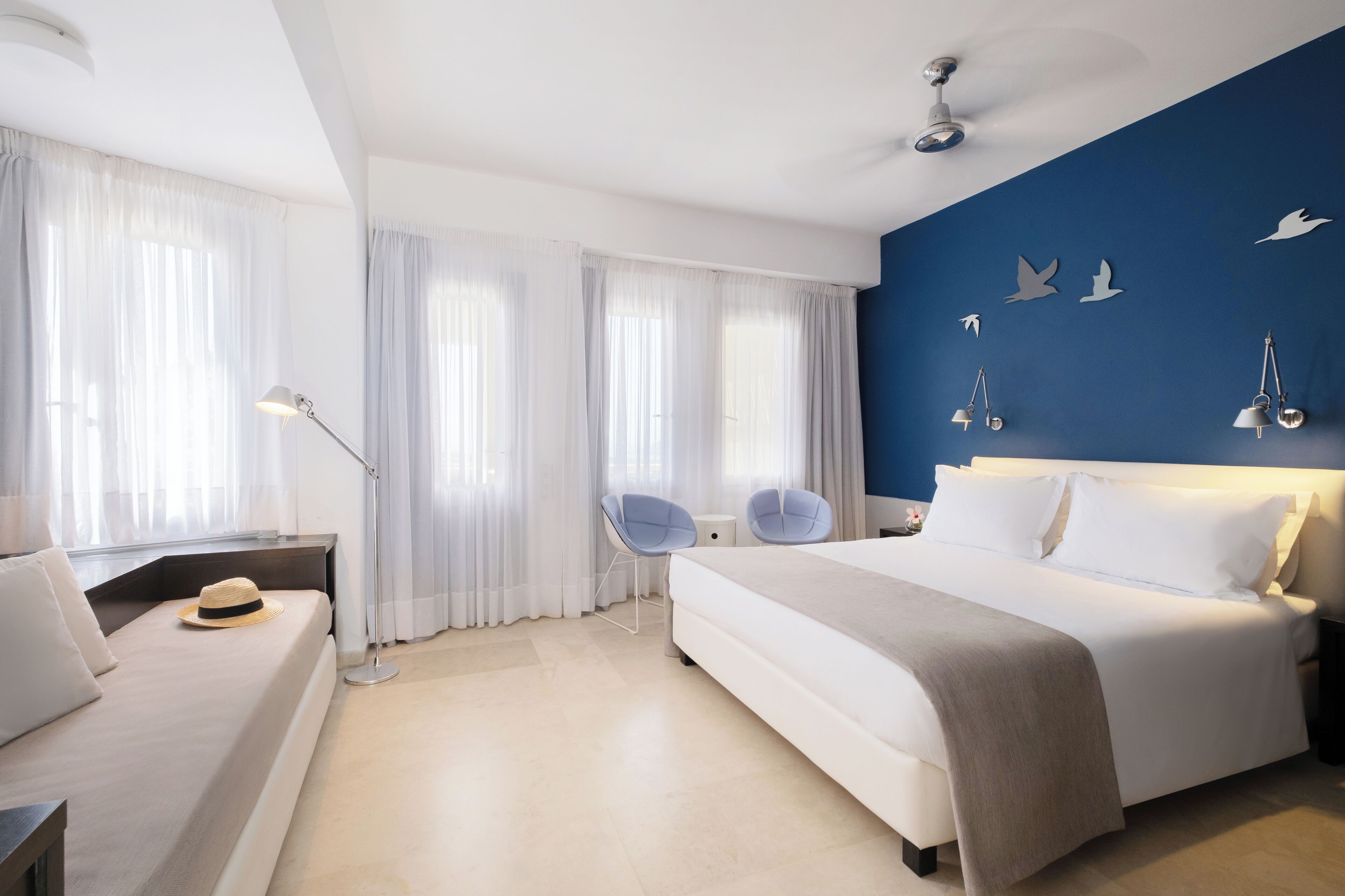 A modern hotel room with a large bed, two chairs, a desk, and a nightstand.