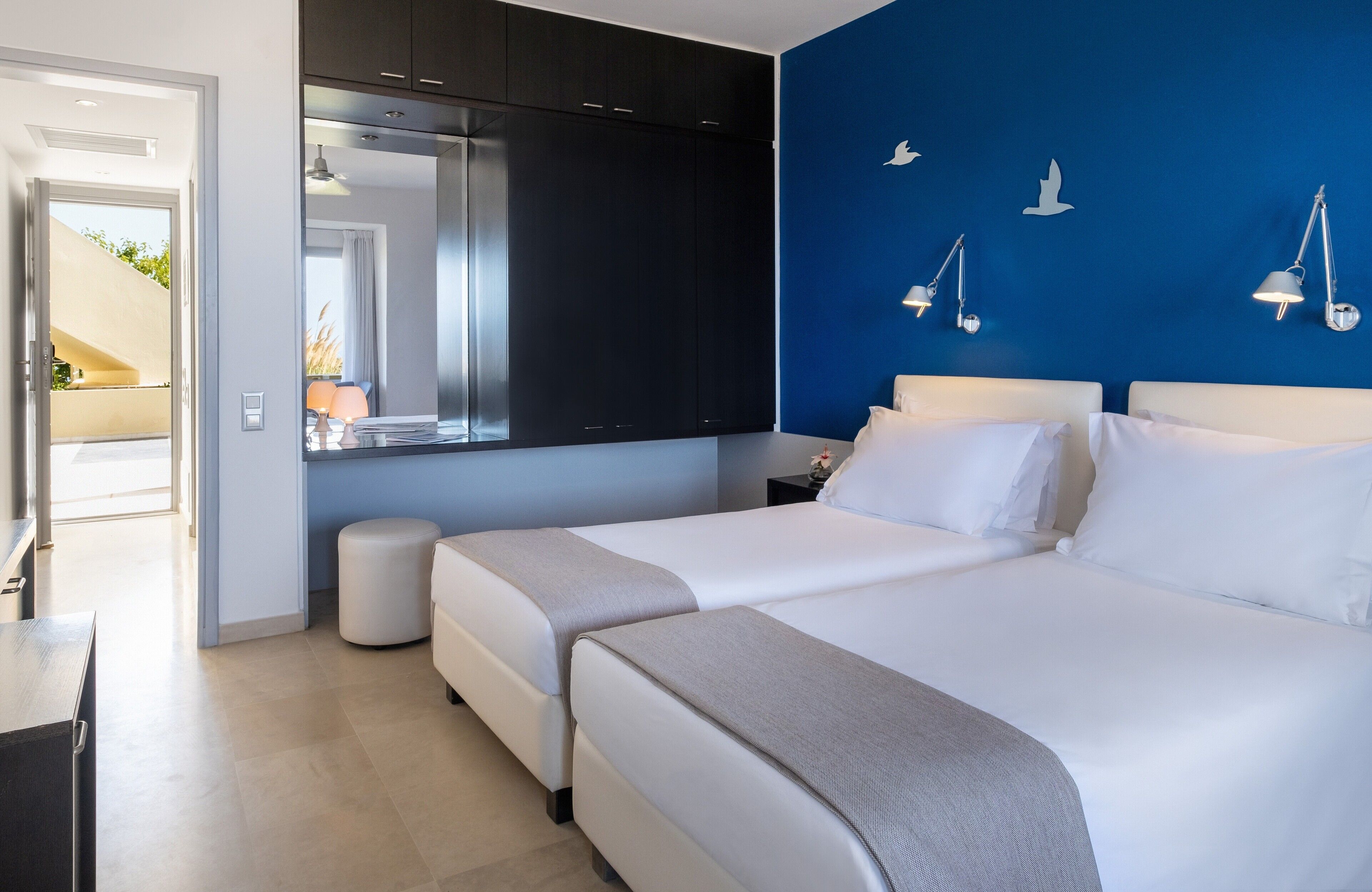 A modern hotel room with two beds, a large mirror, and a blue accent wall.