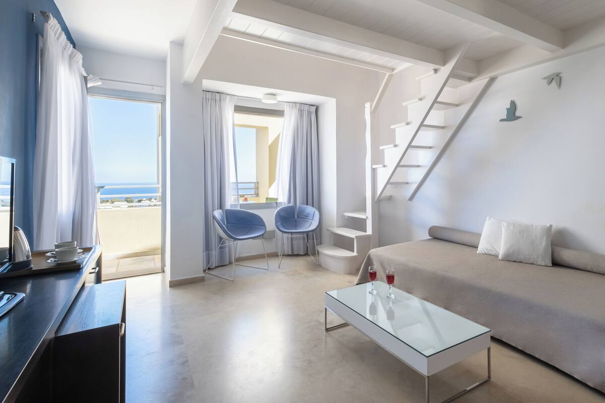 Une chambre d’hôtel moderne dotée d’un balcon, d’un canapé, d’une table basse et d’un bureau avec une chaise.