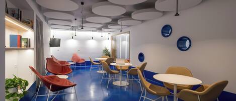 A modern lounge area with round tables and chairs, a flat-screen TV, and a blue floor.