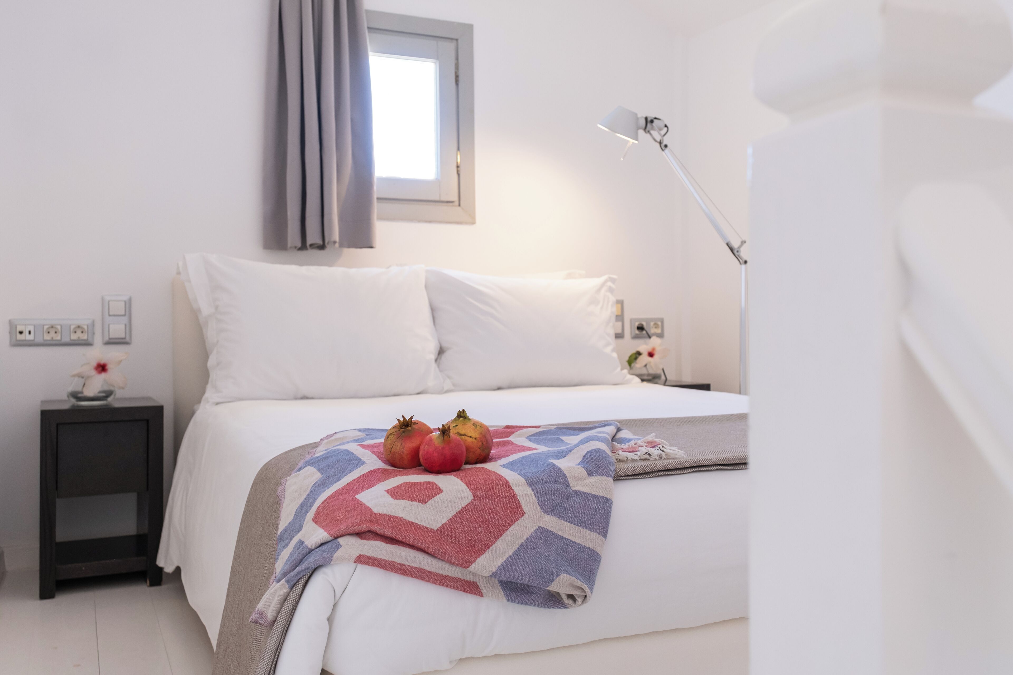 Quarto com cama, mesa de cabeceira, abajur e janela com cortinas.