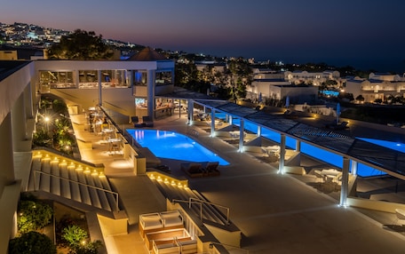 A modern hotel with a pool, outdoor seating, and a view of the city at dusk.