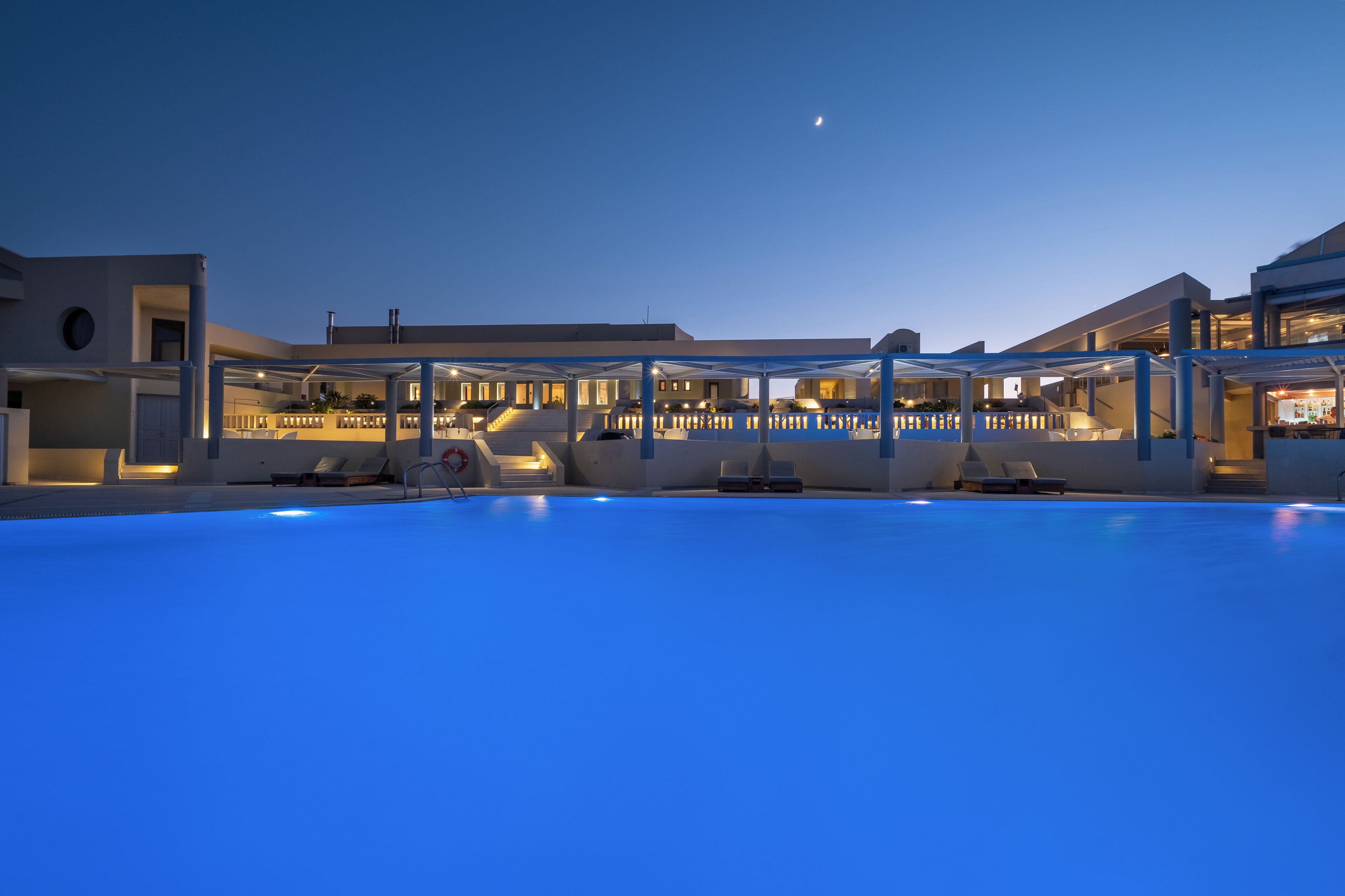 A modern hotel with a swimming pool, outdoor seating, and a covered area.