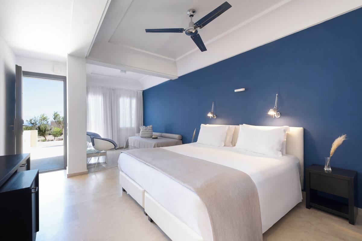Une chambre moderne avec un grand lit, un ventilateur de plafond et une vue sur l’extérieur.