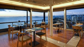 A restaurant with tables and chairs, large windows, and a view of the water.
