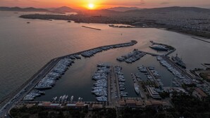 An aerial view of a marina with numerous boats docked, a large ship, and a cityscape in the background during sunset.
