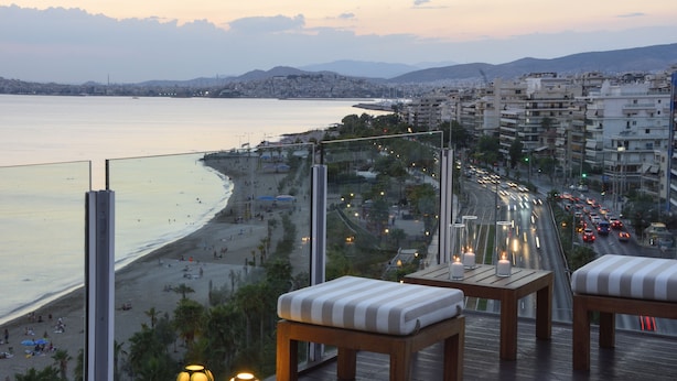 A balcony with wooden furniture and a view of a beach and cityscape.