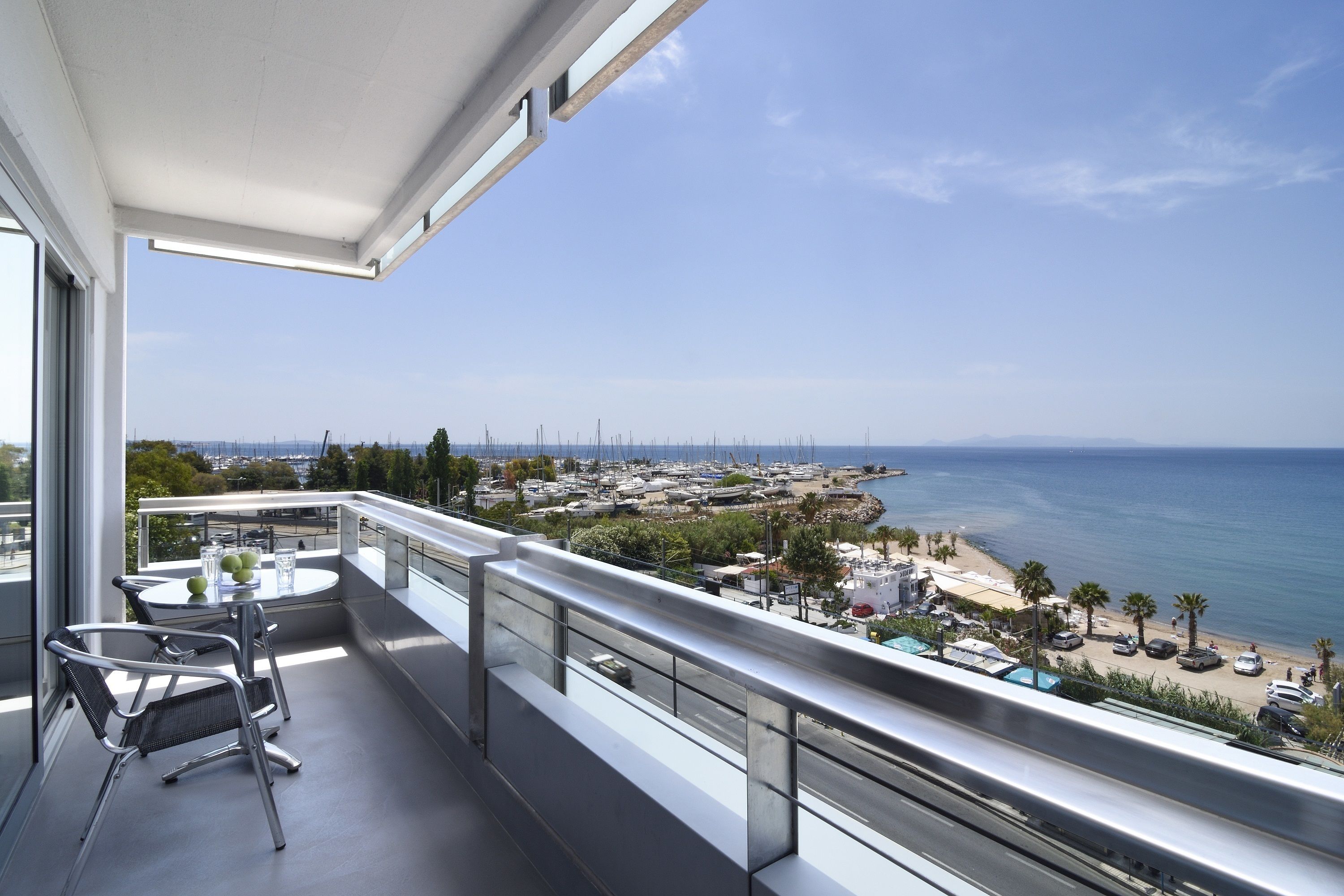 A balcony with a table and chairs, overlooking a marina and beach.