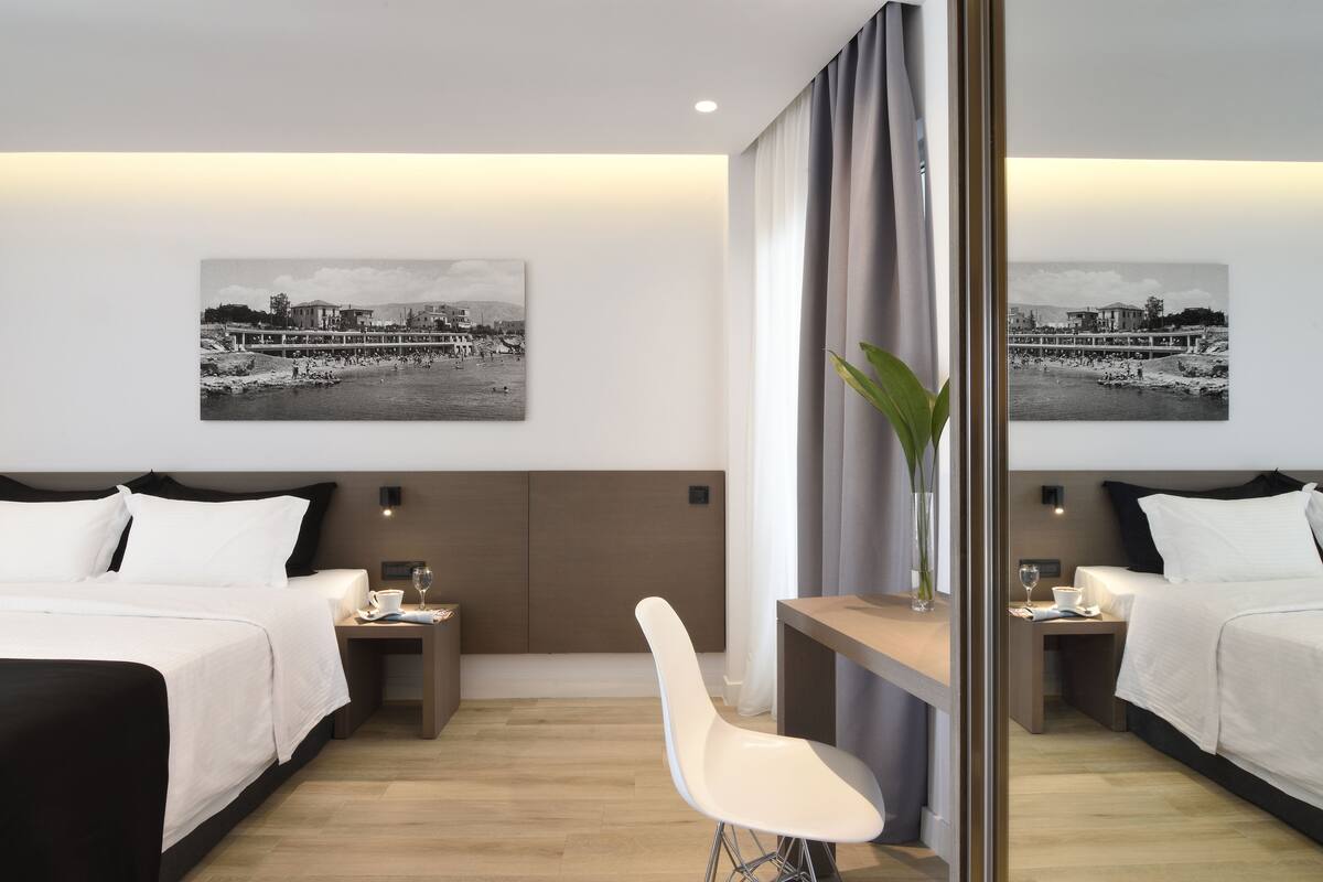 A hotel room with two beds, a small table, a chair, and two nightstands. There are two black and white photographs on the wall.