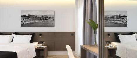 Ett hotellrum med två sängar, ett litet bord, en stol och två sängbord. På väggen hänger två svartvita fotografier.