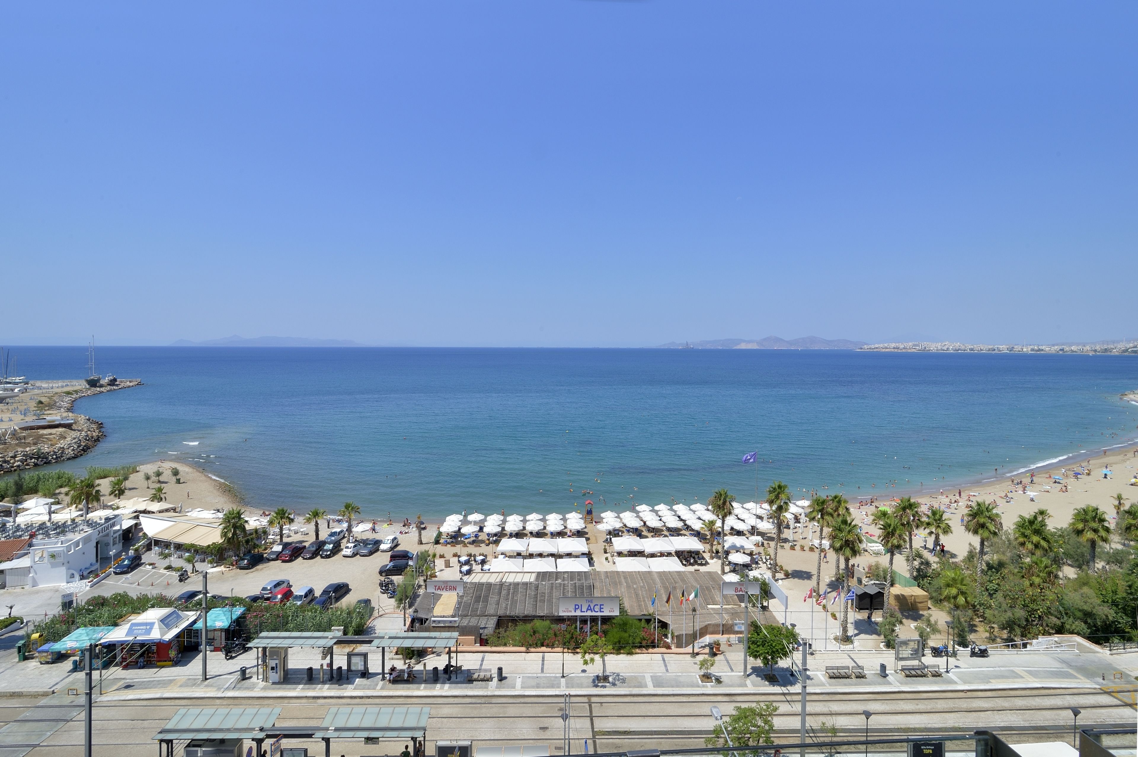 A beachside area with a row of beach umbrellas, a small building labeled 'PLACE', and a parking lot with cars.