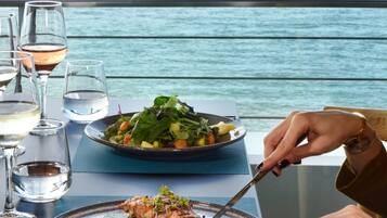 Una mesa con platos de comida y copas de vino, con vista a un cuerpo de agua.