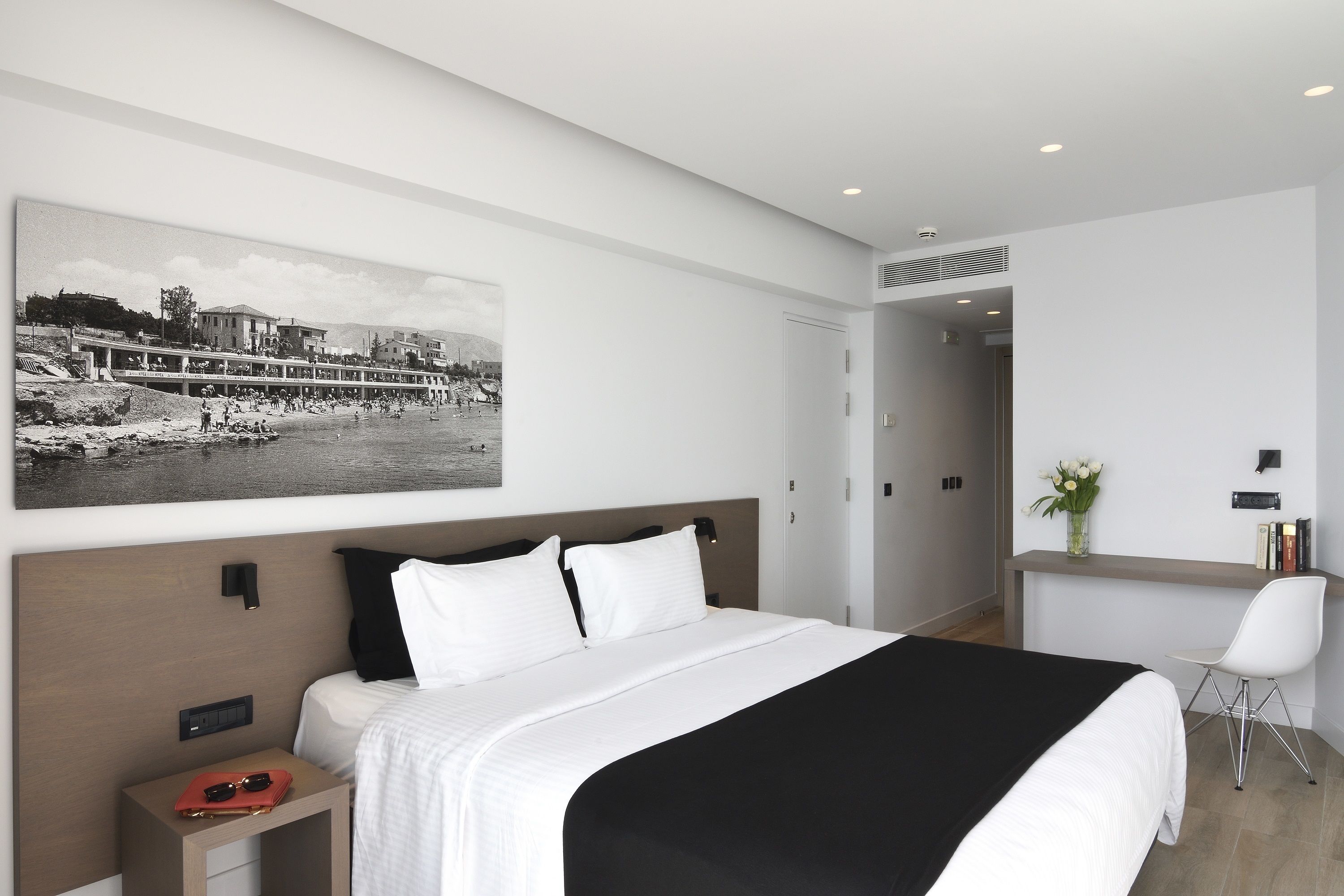 Una habitación de hotel moderna con una cama grande, un escritorio y una silla. Hay un cuadro en la pared y una ventana con vistas a edificios.