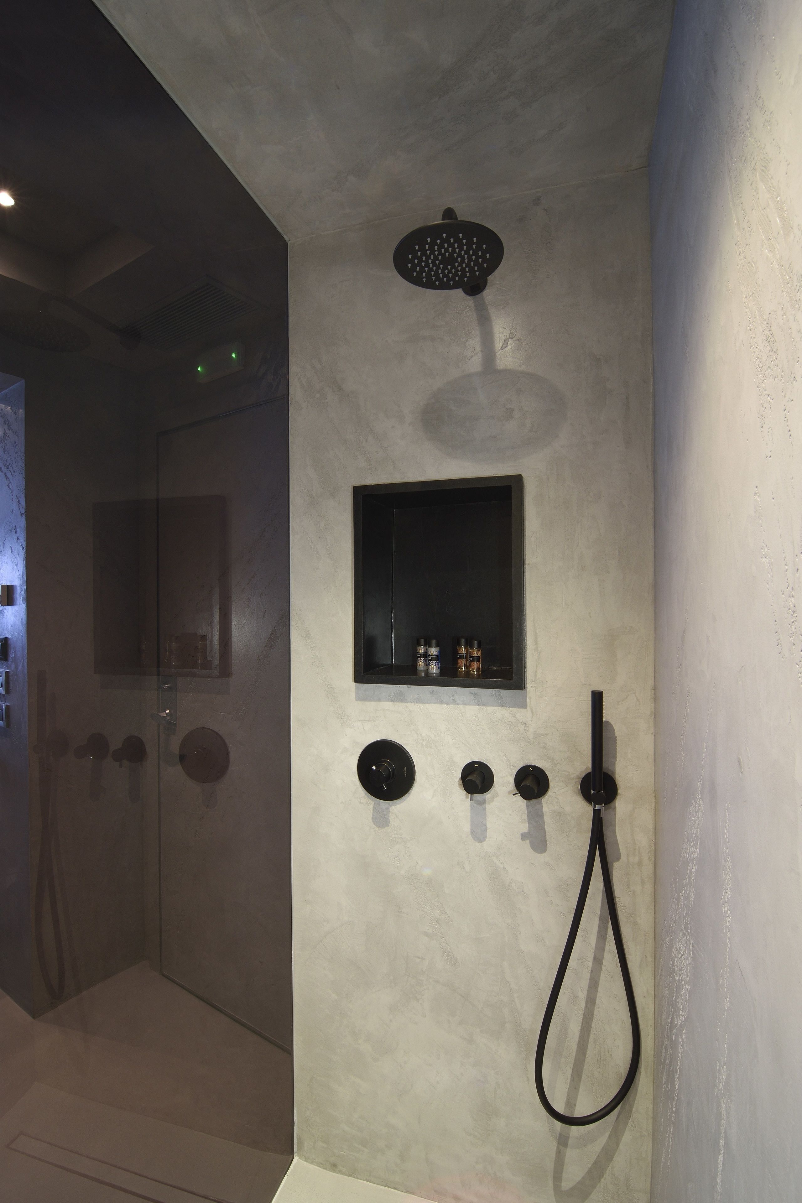 A modern shower area with a handheld showerhead, a wall-mounted control panel, and a small shelf with toiletries.