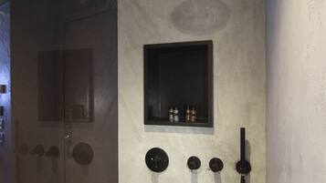 A modern shower area with a handheld showerhead, a wall-mounted control panel, and a small shelf with toiletries.