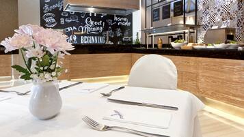 A restaurant setting with a table set for dining, a vase of flowers, and a chalkboard menu in the background.