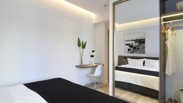 A modern hotel room with a large bed, a desk with a chair, a mirror, and a wardrobe.