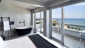 A modern bathroom with a freestanding bathtub, a large window, and a view of the sea.