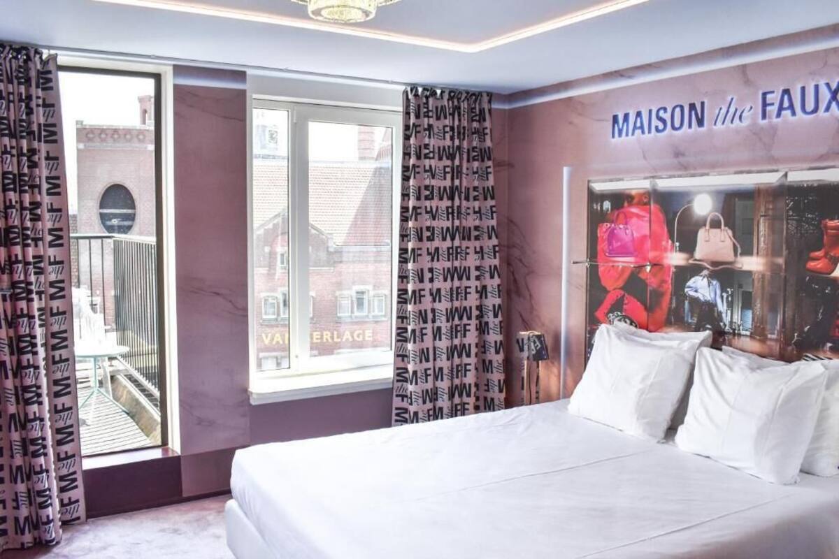 A hotel room with a bed, a window with curtains, and a wall with a Maison de la Faction sign.