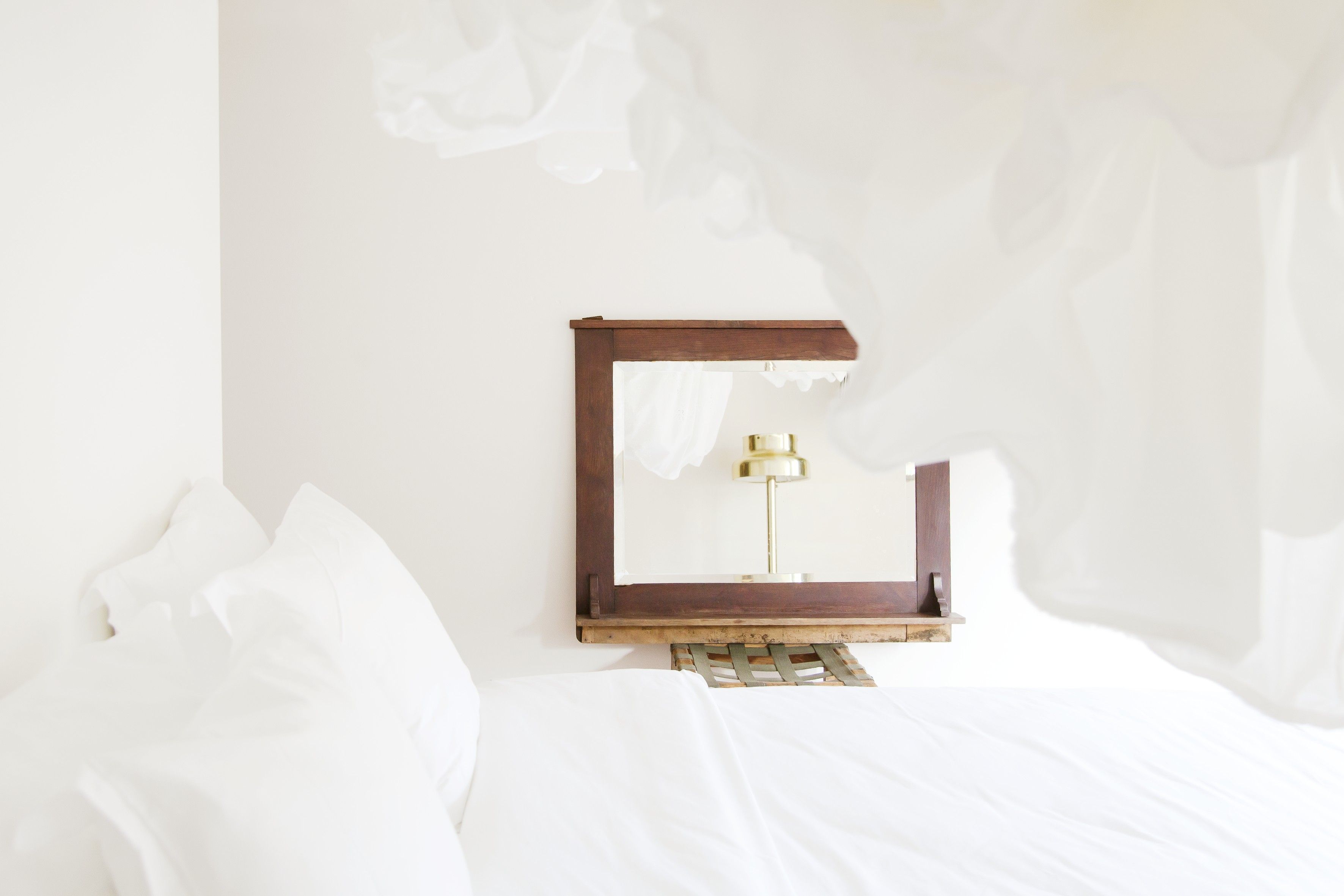 Una cama con sábanas blancas, cabecero de madera y lámpara de noche con base dorada.