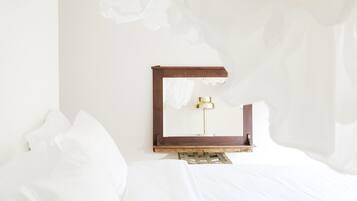 Una cama con sábanas blancas, cabecero de madera y lámpara de noche con base dorada.