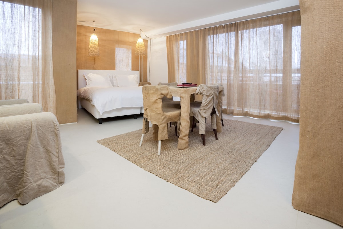 A hotel room with a bed, a dining table with chairs, a rug, and sheer curtains.