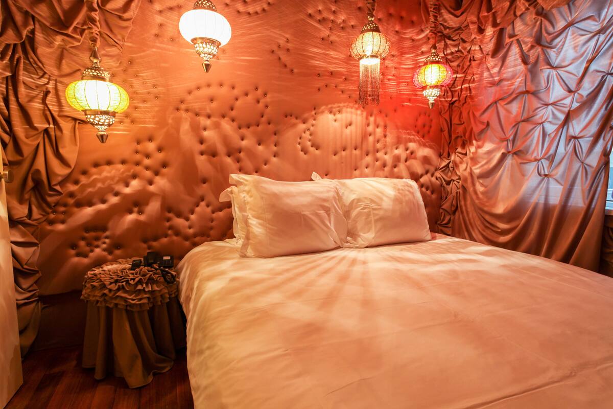 A bedroom with a tufted headboard, a bed with white linens, and decorative hanging lamps.