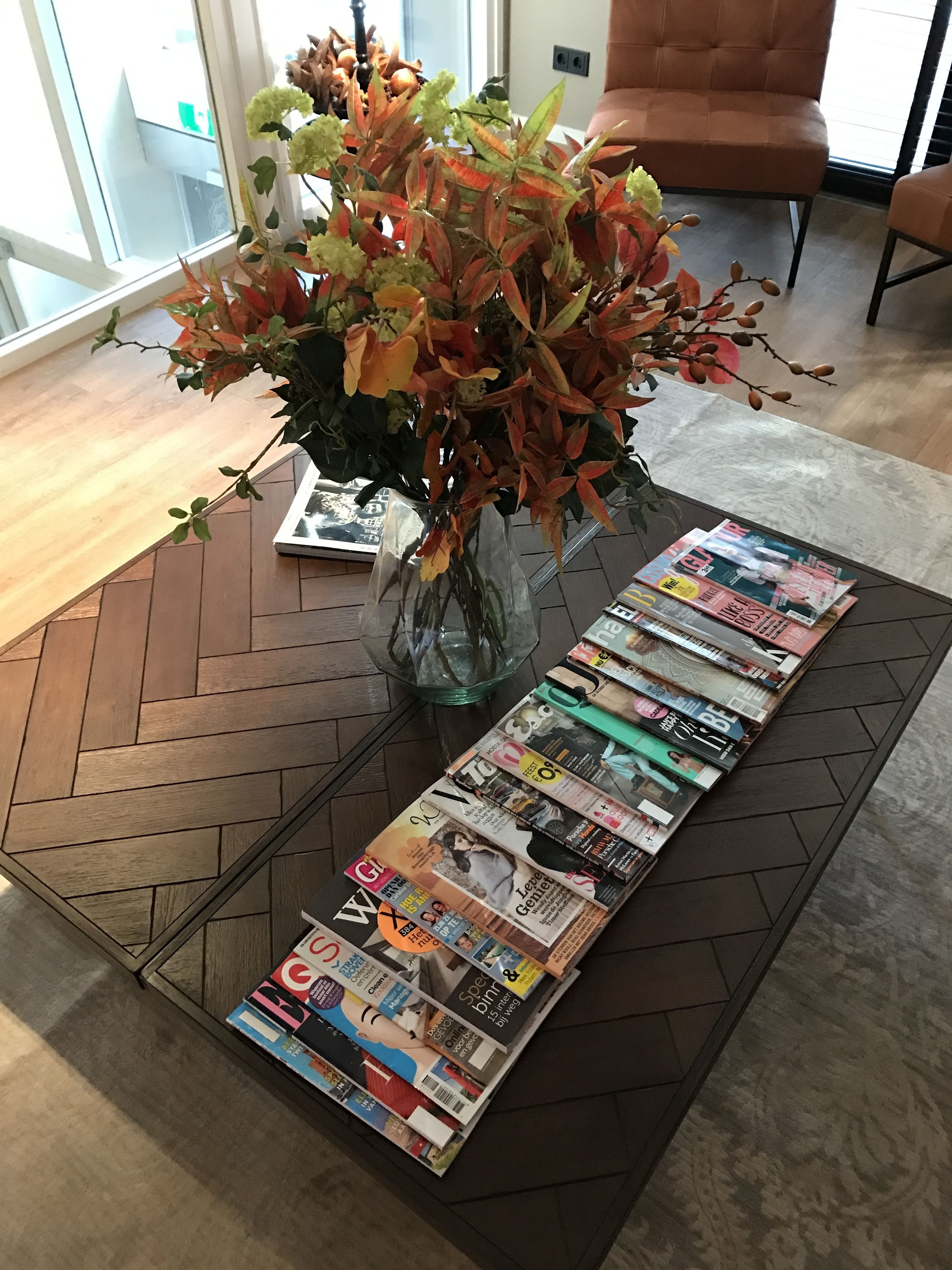 Una sala de estar con una mesa de centro llena de revistas, un jarrón con flores y una silla.