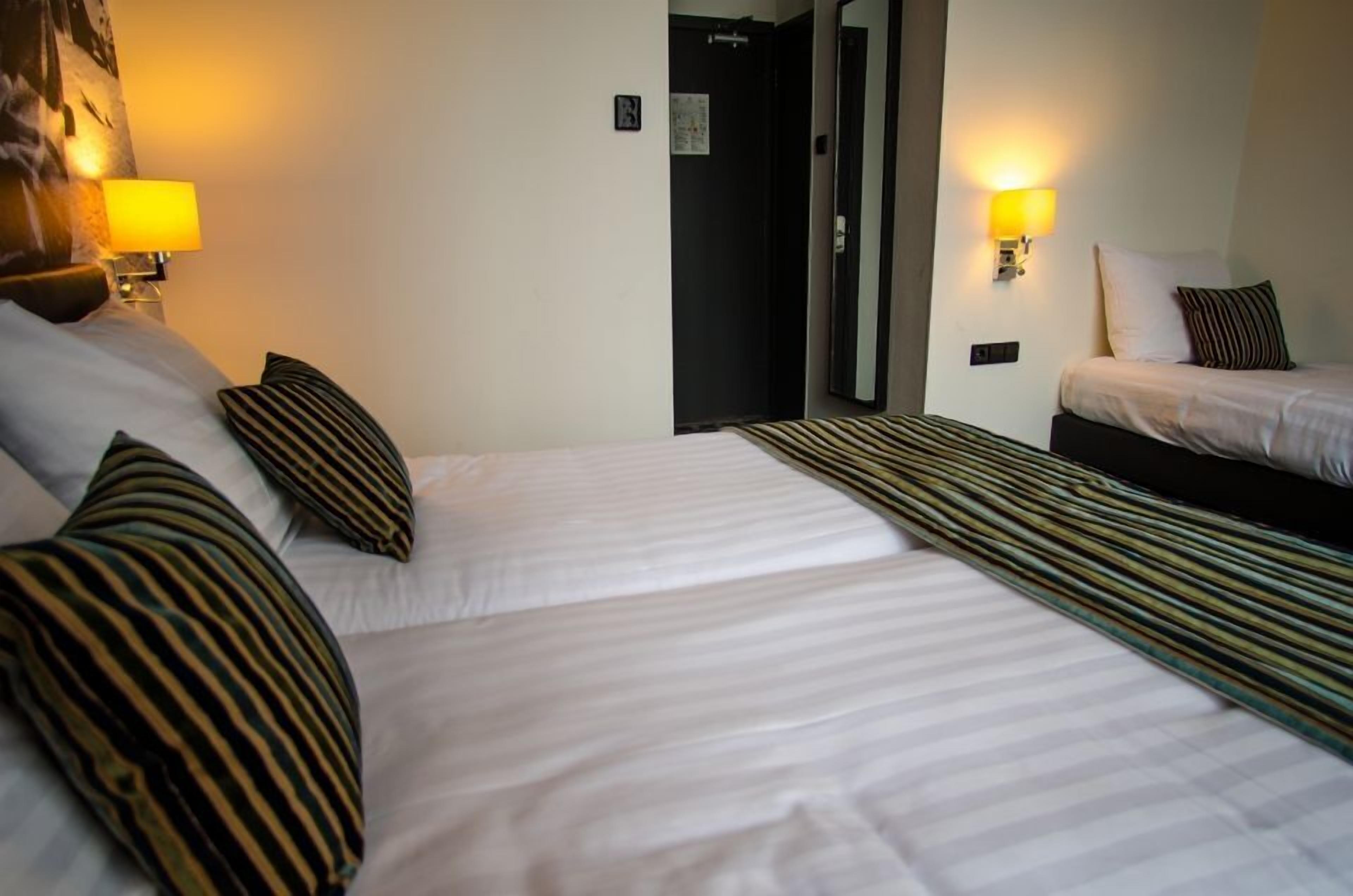 Habitación de hotel con dos camas, almohadas a rayas y lámparas fijadas a la pared.