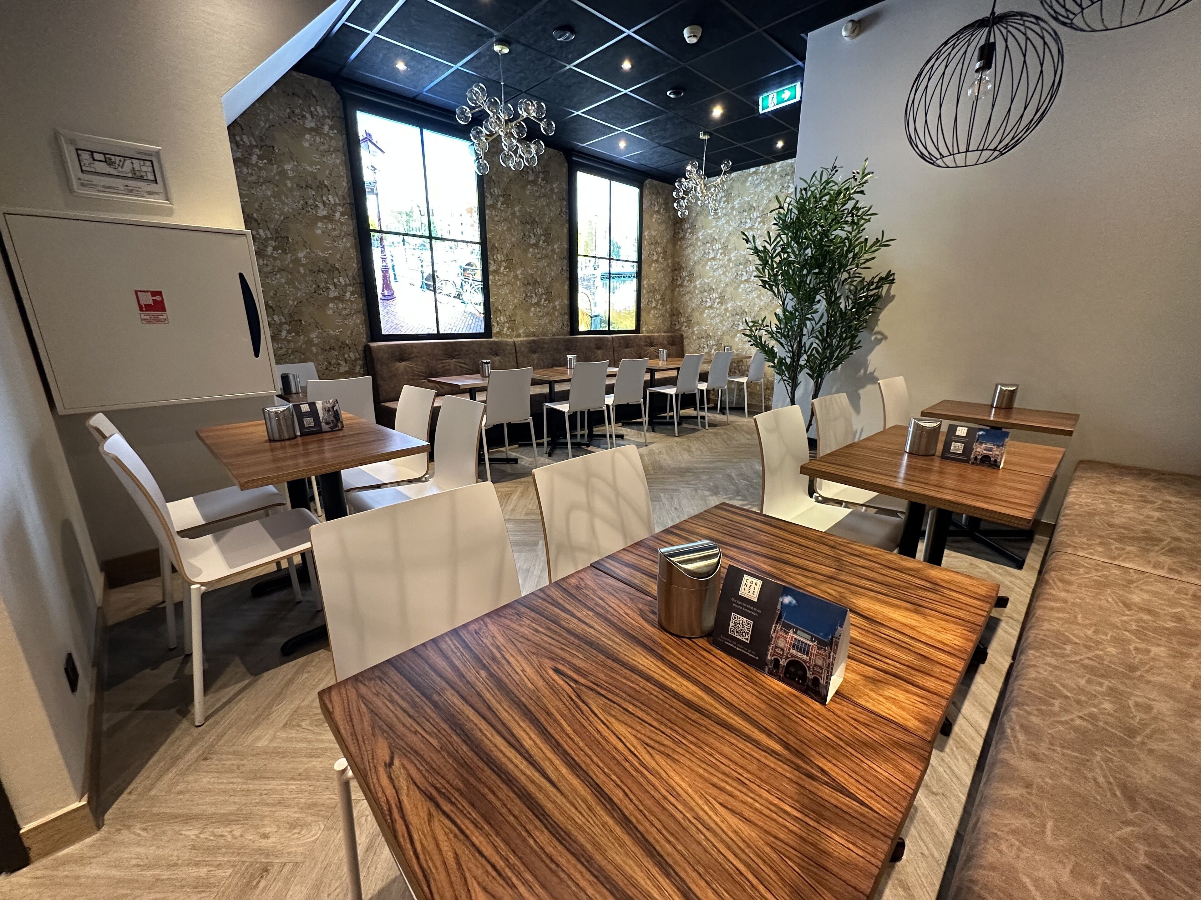 A modern dining area with wooden tables and white chairs, large windows, and a stone wall.