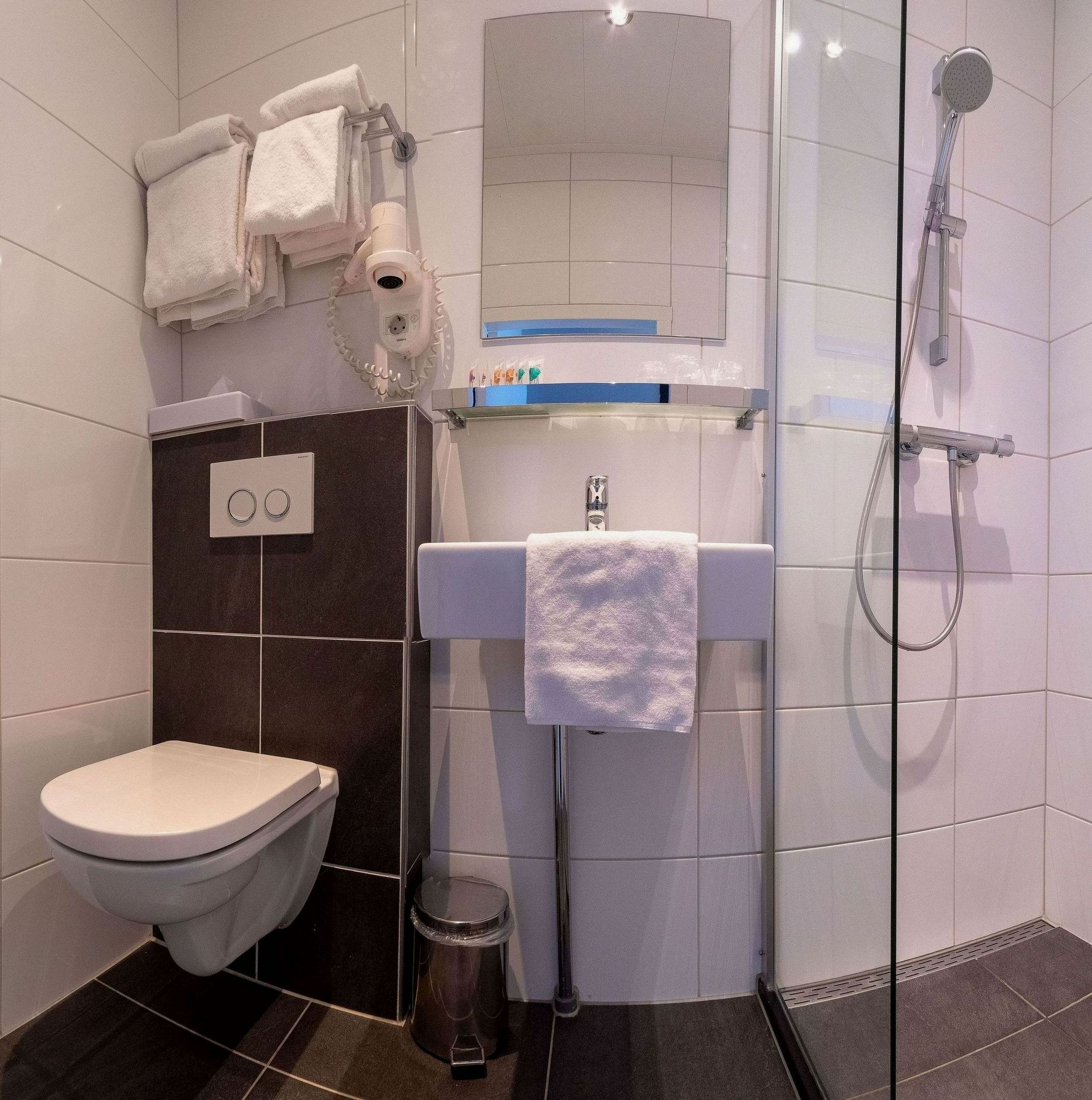 Un baño moderno con inodoro, ducha, lavabo con espejo y toallero con toallas.