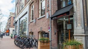 A hotel with a classic brick facade, a black awning, and a sign reading "HOTEL CORNELIUSZ". There are bicycles parked outside and a doormat with the hotel's name.