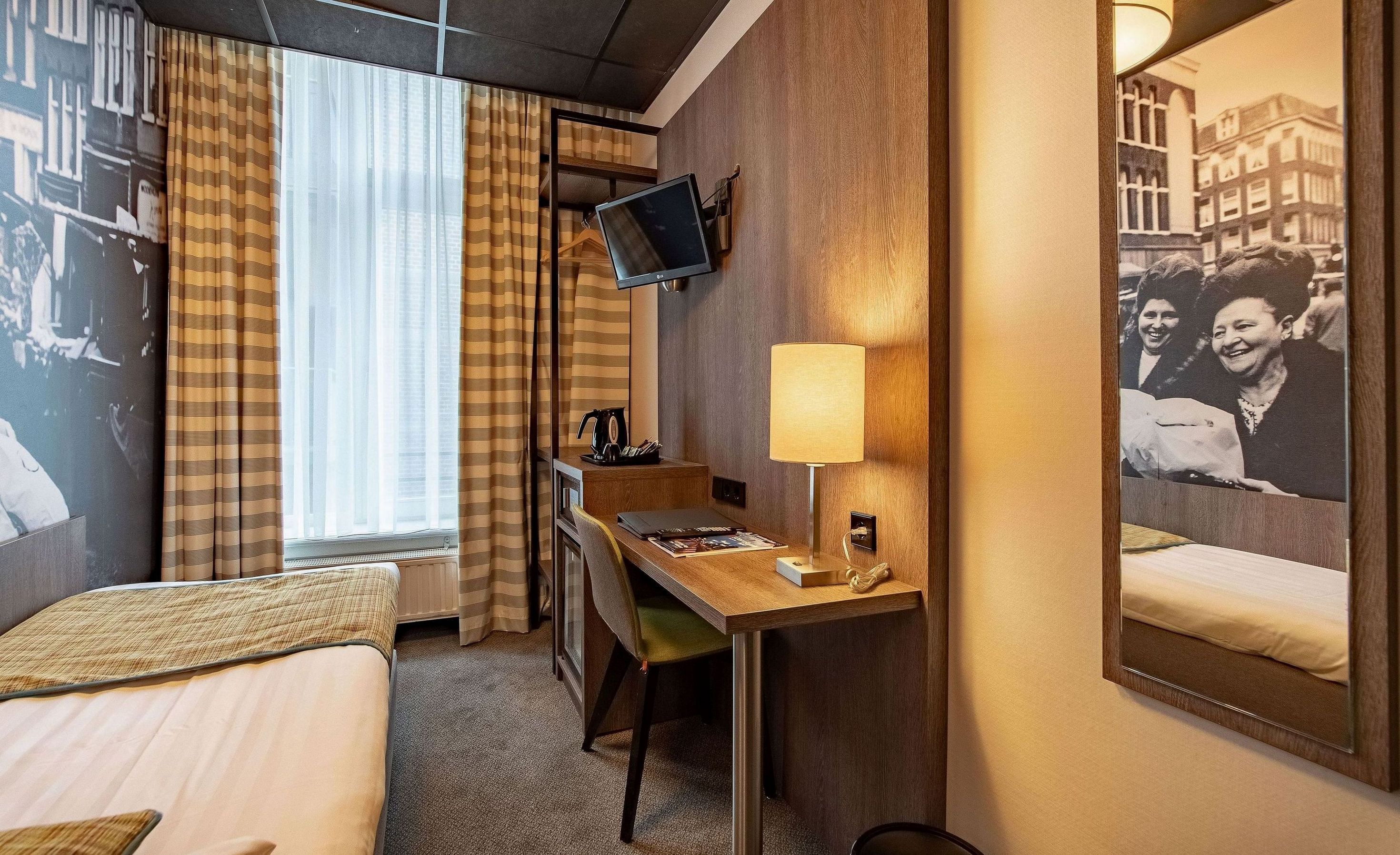 Une chambre d’hôtel avec deux lits, un bureau avec une lampe, une télévision et un tableau encadré au mur.
