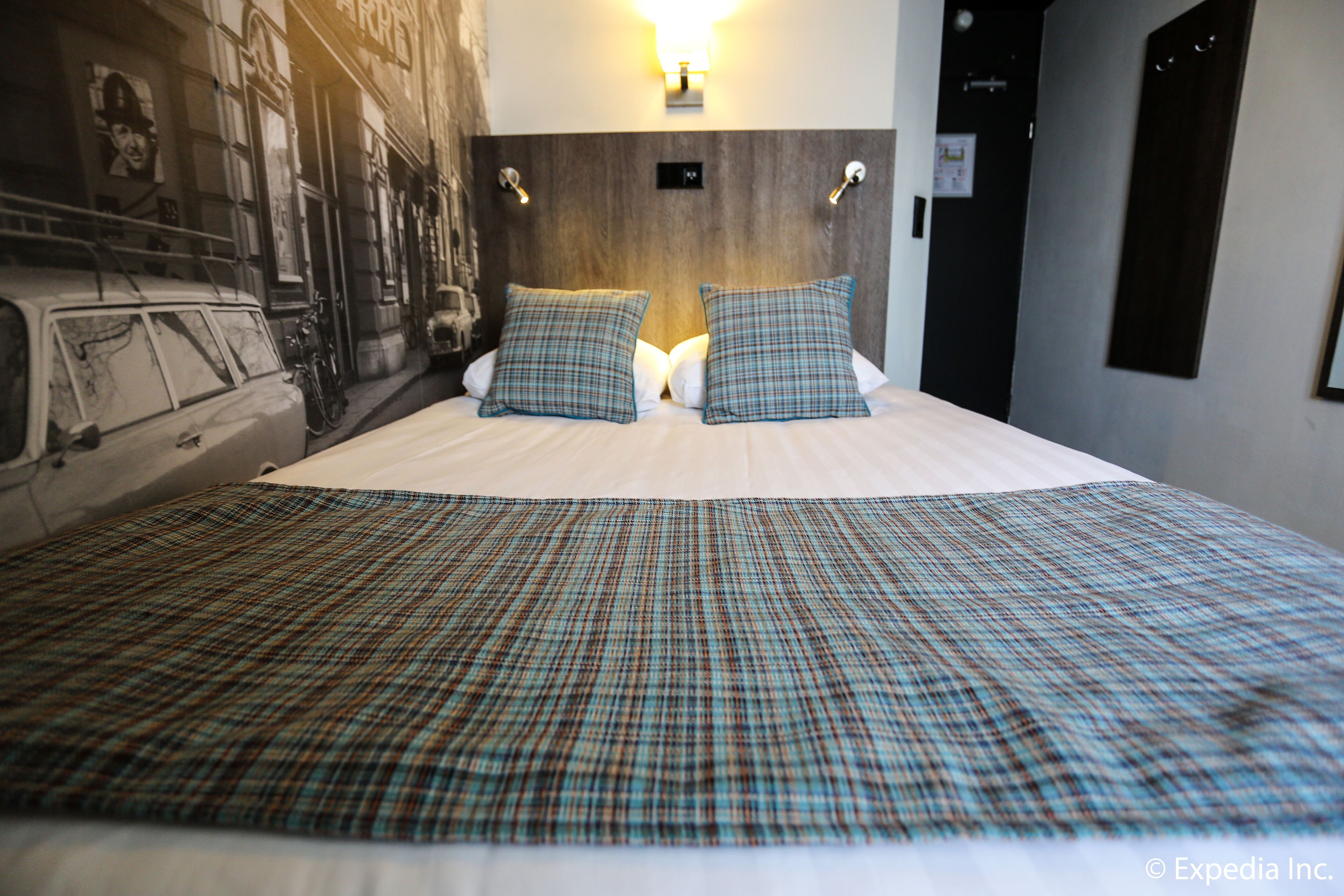 A hotel room with a large bed, two pillows, a headboard, and a wall-mounted light.