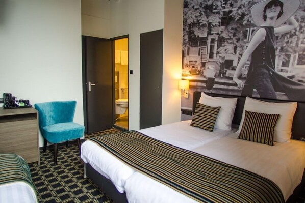 A hotel room with a large bed, a desk, a chair, and a bathroom visible through an open door.
