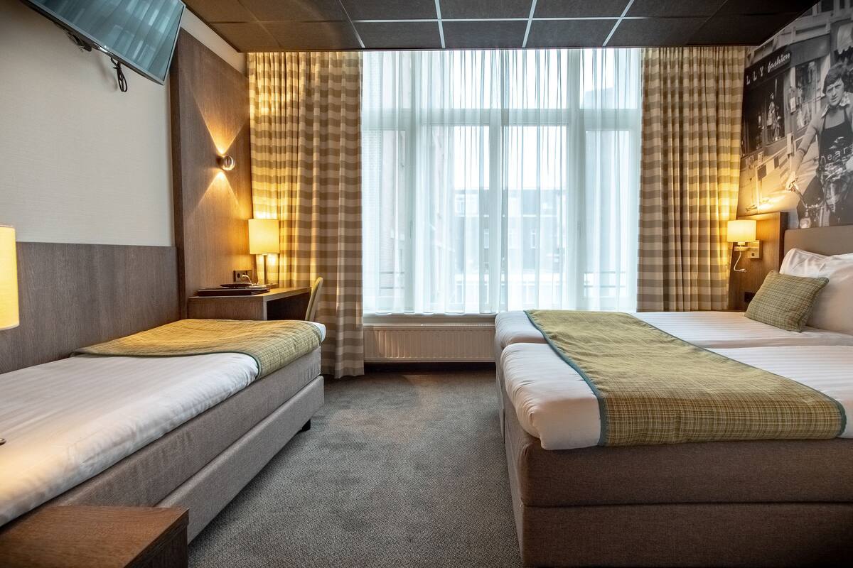 A hotel room with two single beds, a small desk, a chair, and a window with curtains.