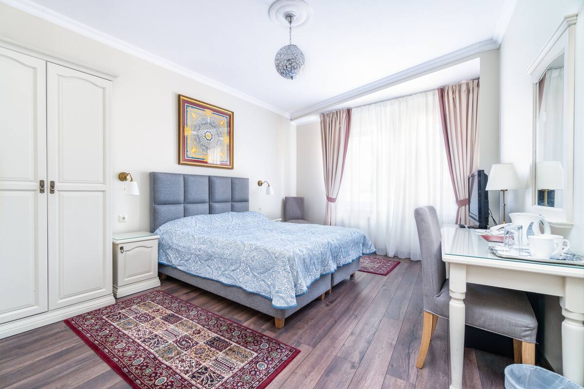 Hotellihuone, jossa on suuri sänky, työpöytä tuolilla, vaatekaappi ja kattokruunu.