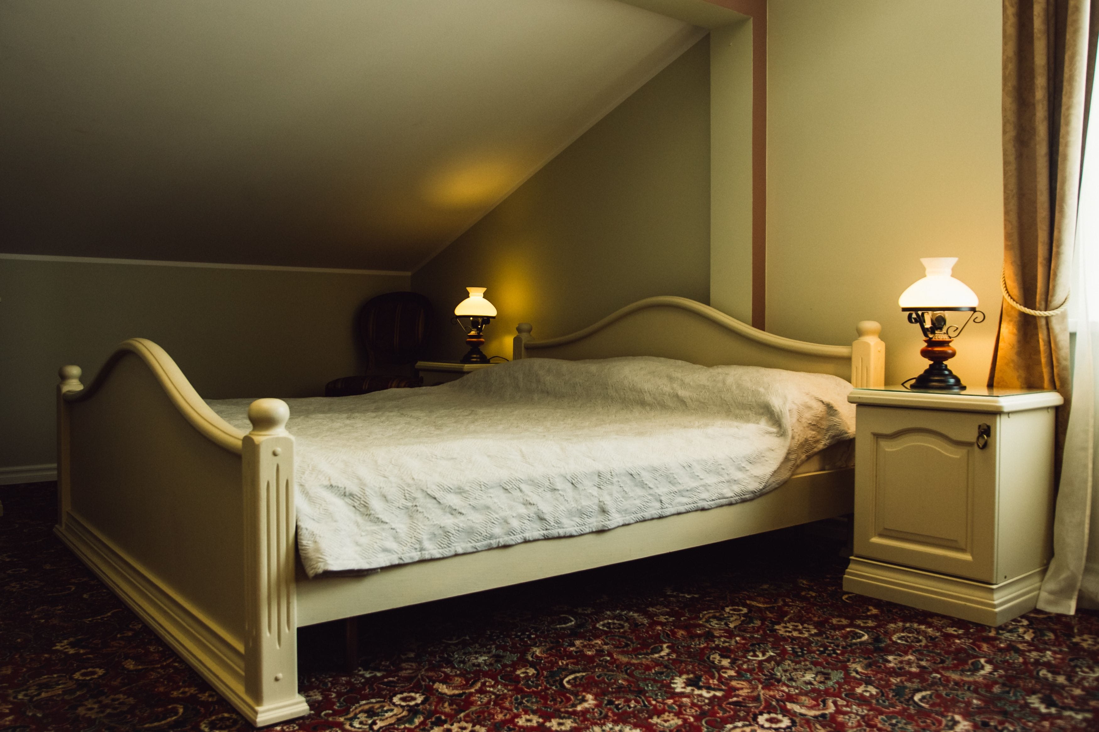 A single bed with a white headboard and footboard, a bedside table with a lamp, and a patterned carpet.