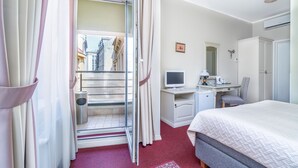 Habitación de hotel con cama, escritorio, silla y vistas a edificios a través de una ventana.