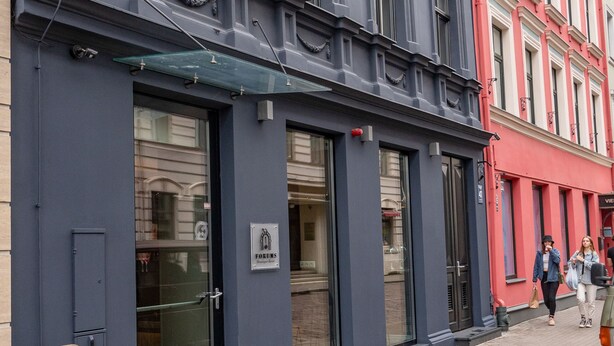 Fachada de un hotel con un letrero destacado, amplias ventanas y un banco de madera en el exterior.