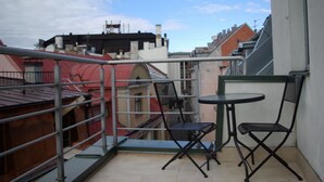 Un balcón con dos sillas y una mesita, con vistas a un paisaje urbano de edificios rojos y blancos.